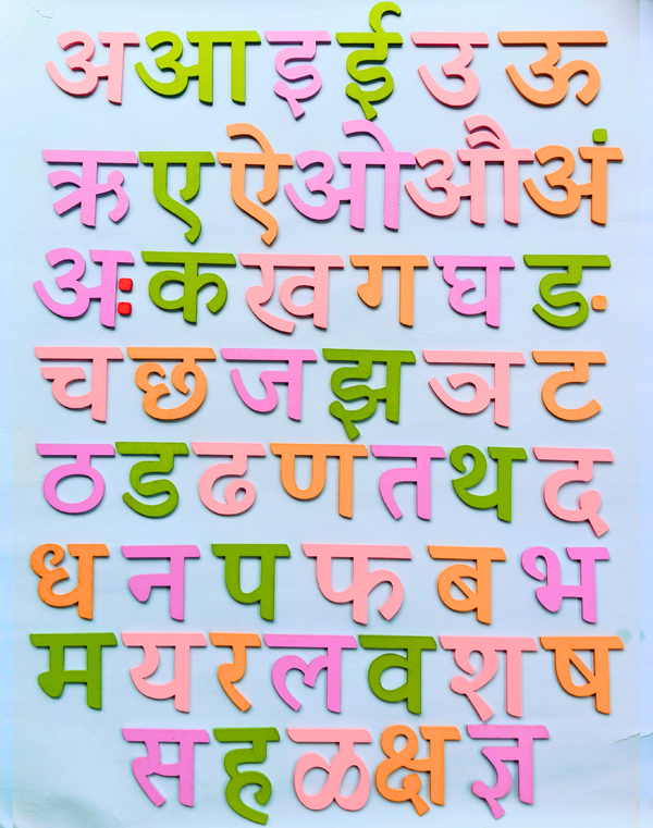 Close-up of a child's hands placing a colorful Marathi letter onto the wooden varnamala board.
