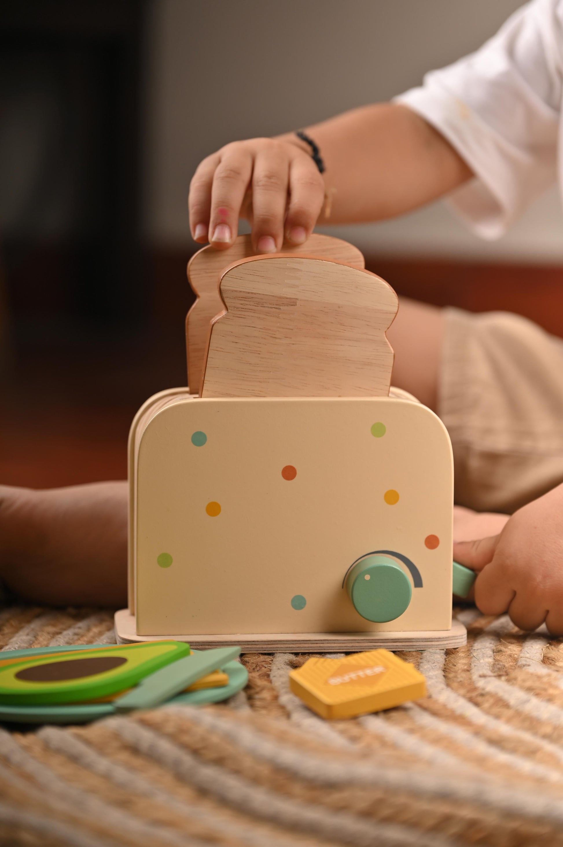 Child's hand playing with a natural wood toaster and pretend breakfast food items
