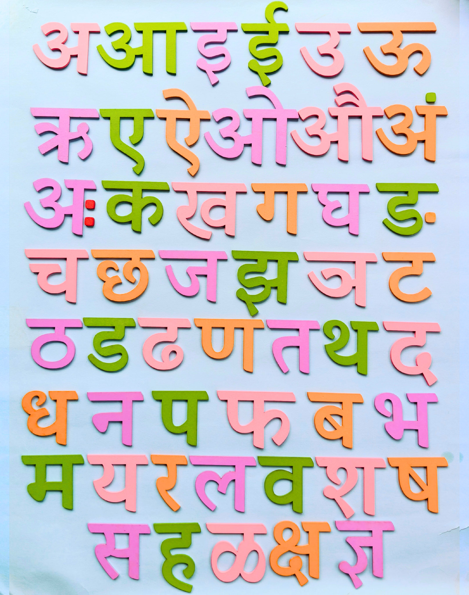 Close-up of a child's hands placing a colorful Marathi letter onto the wooden varnamala board.